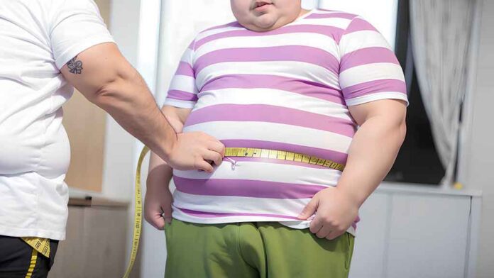 Obese boy measures his fat belly with a measuring tape in clinic